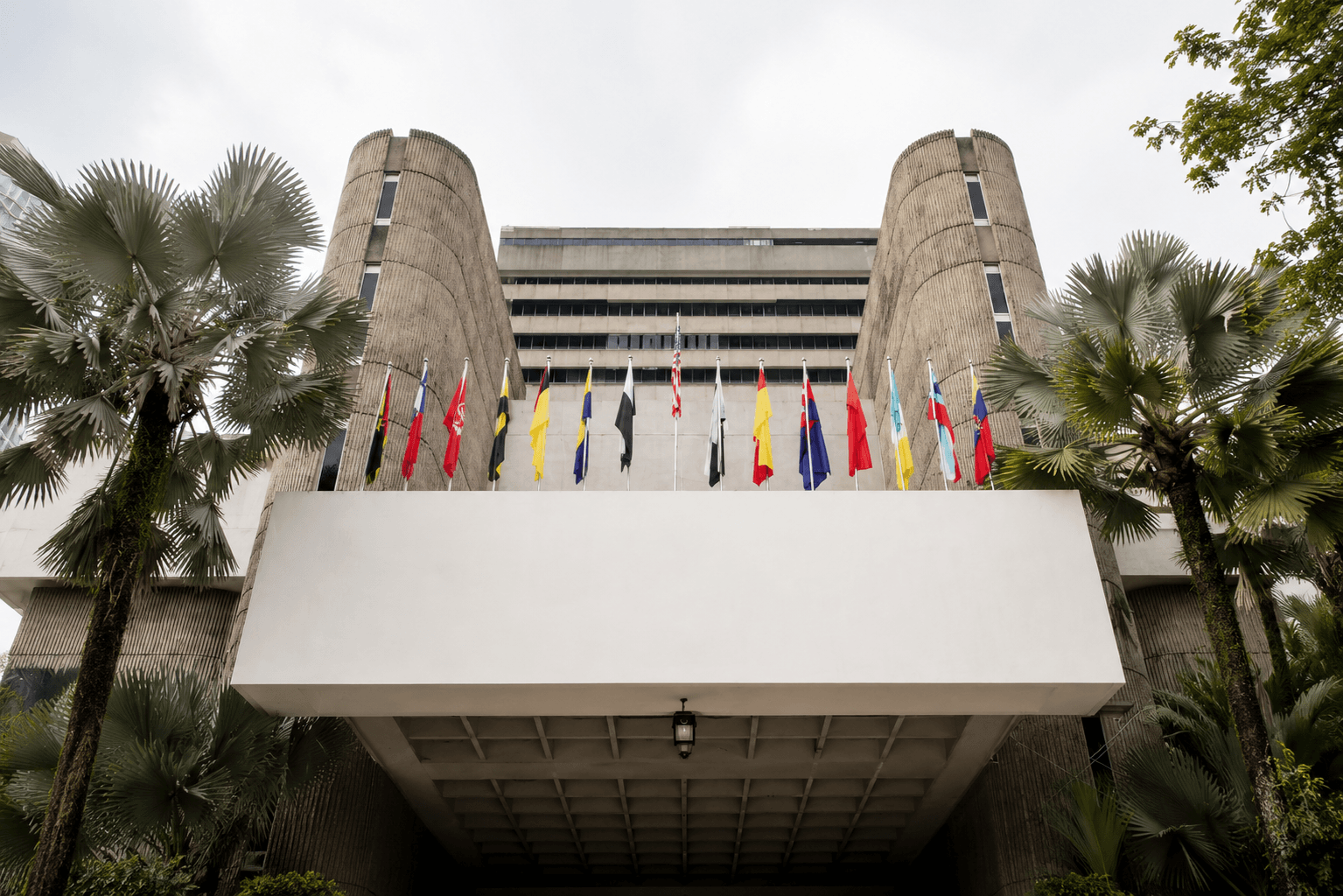 A Malaysian institutional building framed by palm trees and flags